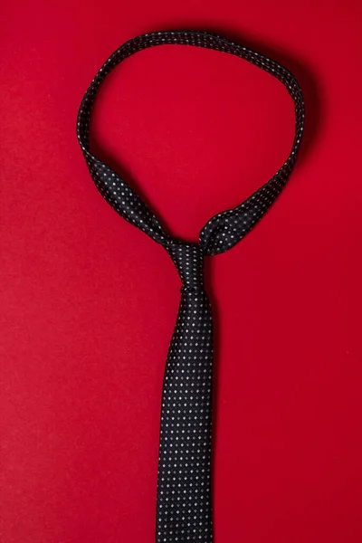 Black men's tie. Tie on a red background. Male style. Classic men's fashion