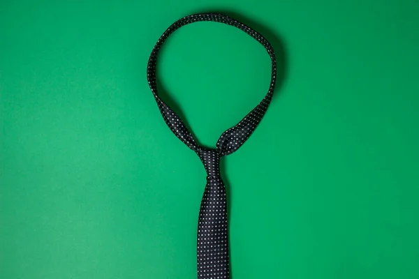 Black men's tie. Tie on a green background. Male style. Classic men's fashion