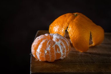 Ahşap bir yüzeyde soyulmuş mandalina. Citrus meyvesi. Mandalina kabuğunun yanında soyulmuş bir mandalina yatar..