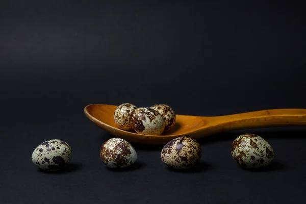 Quail eggs on a black background. Healthy food. Quail eggs lie in a wooden spoon, several eggs lie side by side