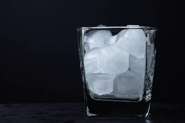 Ice in a glass on a black background. Pieces of ice. Whiskey glass