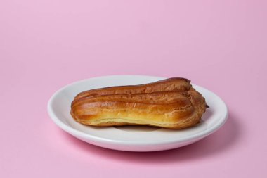 Pembe arka planda ekler. Beyaz bir tabakta bir ekkin. Tatlı kahvaltı..