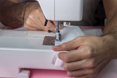 Pembe arka planda beyaz dikiş makinesi. Elektrikli dikiş makinesi. Dikiş makinesinde çalışmak için eller havaya. El yapımı bir alet. Dikiş işi.