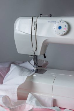 Pembe arka planda beyaz dikiş makinesi. Elektrikli dikiş makinesi. Dikiş makinesindeki beyaz kumaş. El yapımı bir alet. Dikiş işi.