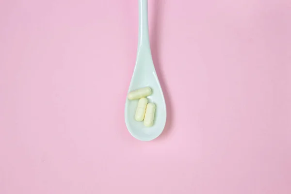 ピンクの背景に丸薬と白いスプーン 健康の概念 — ストック写真