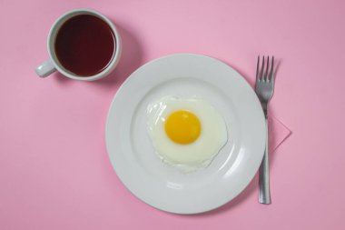 Pembe arka planda çırpılmış yumurta. Beyaz tabakta sahanda yumurta. Bir fincan kahveyle nefis bir kahvaltı.