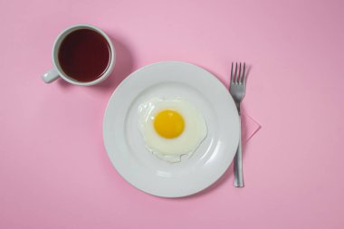 Pembe arka planda çırpılmış yumurta. Beyaz tabakta sahanda yumurta. Bir fincan kahveyle nefis bir kahvaltı.