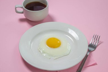 Pembe arka planda çırpılmış yumurta. Beyaz tabakta sahanda yumurta. Bir fincan kahveyle nefis bir kahvaltı.