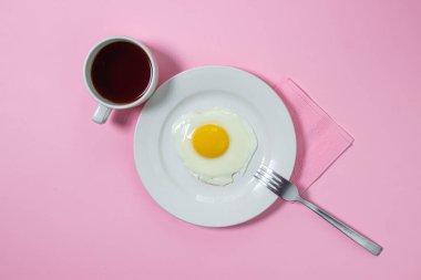 Pembe arka planda çırpılmış yumurta. Beyaz tabakta sahanda yumurta. Bir fincan kahveyle nefis bir kahvaltı.