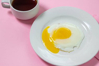 Pembe arka planda çırpılmış yumurta. Beyaz tabakta sahanda yumurta. Bir fincan kahveyle nefis bir kahvaltı.