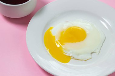 Pembe arka planda çırpılmış yumurta. Beyaz tabakta sahanda yumurta. Bir fincan kahveyle nefis bir kahvaltı.
