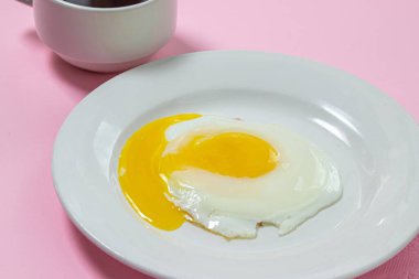 Pembe arka planda çırpılmış yumurta. Beyaz tabakta sahanda yumurta. Bir fincan kahveyle nefis bir kahvaltı.