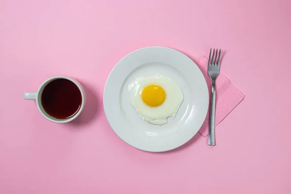 Scrambled eggs on a pink background. Fried eggs on a white plate. Delicious breakfast with a cup of coffee.