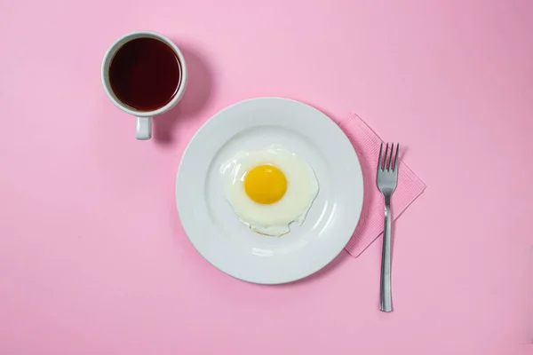 Scrambled eggs on a pink background. Fried eggs on a white plate. Delicious breakfast with a cup of coffee.