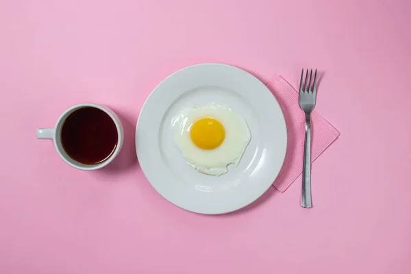 Scrambled eggs on a pink background. Fried eggs on a white plate. Delicious breakfast with a cup of coffee.