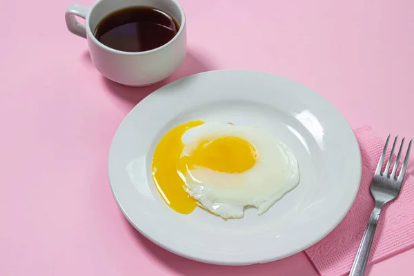 Scrambled eggs on a pink background. Fried eggs on a white plate. Delicious breakfast with a cup of coffee.