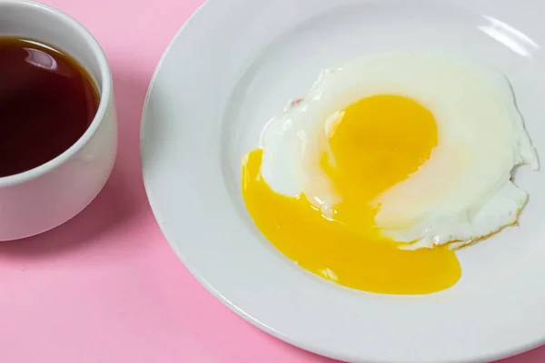 Scrambled eggs on a pink background. Fried eggs on a white plate. Delicious breakfast with a cup of coffee.