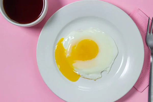 Scrambled eggs on a pink background. Fried eggs on a white plate. Delicious breakfast with a cup of coffee.