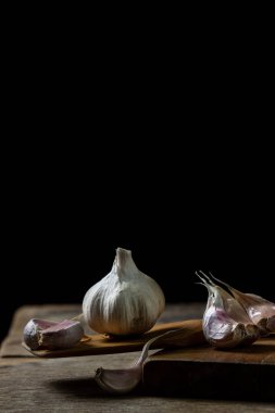 Siyah arka planda sarımsak. Sarımsağın yanında sarımsak ezmesi. Tahta bir spatulada sarımsak.