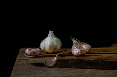 Siyah arka planda sarımsak. Sarımsağın yanında sarımsak ezmesi. Tahta bir spatulada sarımsak.