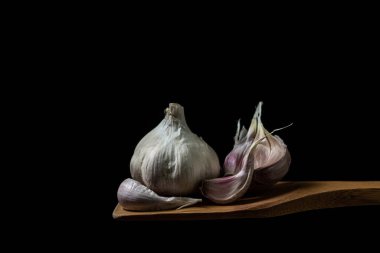 Siyah arka planda sarımsak. Sarımsağın yanında sarımsak ezmesi. Tahta bir spatulada sarımsak.