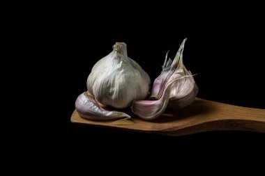 Siyah arka planda sarımsak. Sarımsağın yanında sarımsak ezmesi. Tahta bir spatulada sarımsak.