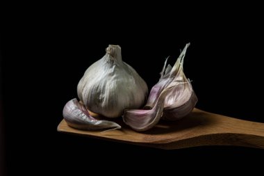 Siyah arka planda sarımsak. Sarımsağın yanında sarımsak ezmesi. Tahta bir spatulada sarımsak.