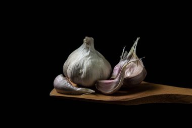 Siyah arka planda sarımsak. Sarımsağın yanında sarımsak ezmesi. Tahta bir spatulada sarımsak.