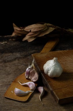 Siyah arka planda sarımsak. Sarımsağın yanında sarımsak ezmesi. Tahta bir spatulada sarımsak.