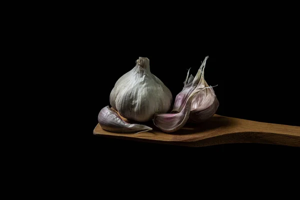 Garlic on a black background. Garlic cloves next to whole garlic. Garlic on a wooden spatula
