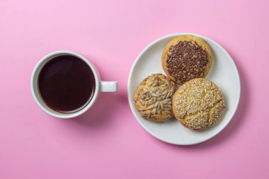 Pembe arka planda kurabiyeler. Beyaz tabakta serpiştirilmiş karamelli kurabiyeler. Tatlının yanında bir fincan kahve.