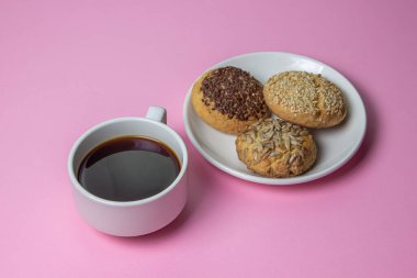 Pembe arka planda kurabiyeler. Beyaz tabakta serpiştirilmiş karamelli kurabiyeler. Tatlının yanında bir fincan kahve.