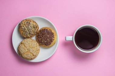 Pembe arka planda kurabiyeler. Beyaz tabakta serpiştirilmiş karamelli kurabiyeler. Tatlının yanında bir fincan kahve.