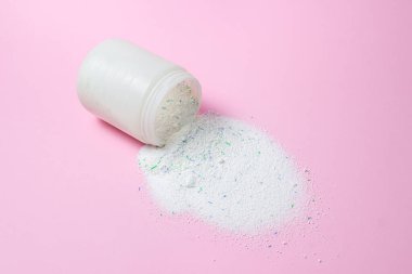 Laundry detergent on a pink background. Washing powder spilled out of the measuring cup. Household chemicals
