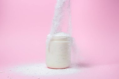 Laundry detergent on a pink background. The washing powder is poured into a measuring cup. Household chemicals
