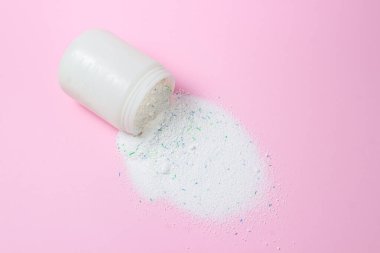 Laundry detergent on a pink background. Washing powder spilled out of the measuring cup. Household chemicals