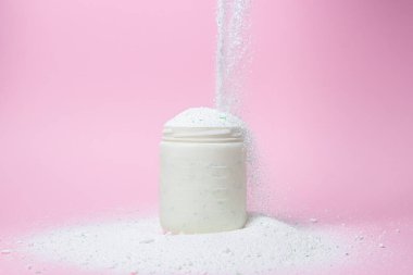 Laundry detergent on a pink background. The washing powder is poured into a measuring cup. Household chemicals