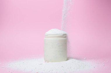 Laundry detergent on a pink background. The washing powder is poured into a measuring cup. Household chemicals