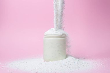 Laundry detergent on a pink background. The washing powder is poured into a measuring cup. Household chemicals