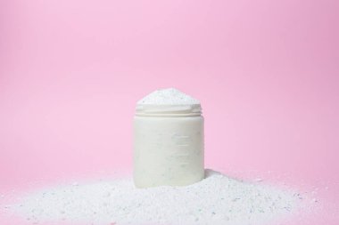 Laundry detergent on a pink background. Measuring cup overflowing with detergent. Household chemicals