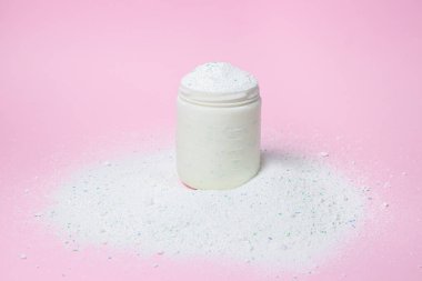 Laundry detergent on a pink background. Measuring cup overflowing with detergent. Household chemicals
