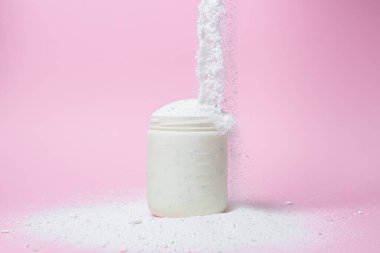 Laundry detergent on a pink background. The washing powder is poured into a measuring cup. Household chemicals