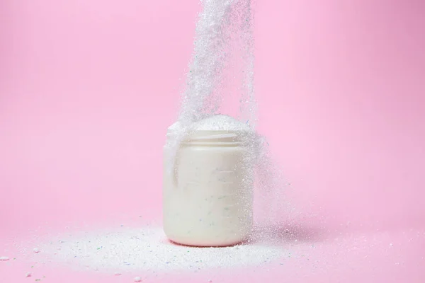 Laundry detergent on a pink background. The washing powder is poured into a measuring cup. Household chemicals
