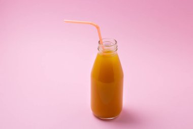 Pembe arka planda meyve suyu olan cam şişe. Doğal mango suyu. Tazeleyici içecek.