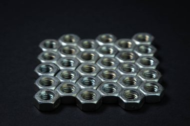 Siyah arka planda fındık cıvataları. sivri uçlu. Fındık cıvataları birkaç sıra halinde düzgünce dizilmiş.