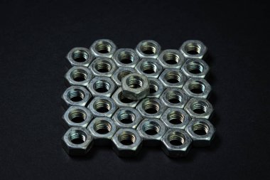 Siyah arka planda fındık cıvataları. sivri uçlu. Fındık cıvataları birkaç sıra halinde düzgünce istiflenmiş, sıralar birbirine çok yakın. Bir fındık diğerinin üstünde.