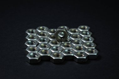 Siyah arka planda fındık cıvataları. sivri uçlu. Fındık cıvataları birkaç sıra halinde düzgünce istiflenmiş, sıralar birbirine çok yakın. Bir fındık diğerinin üstünde.