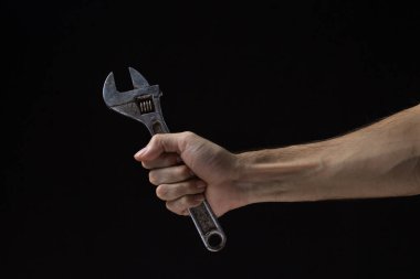 Siyah arka planda ayarlanabilir anahtar. Eski bir iş aleti. Bir adamın eli ayarlanabilir bir anahtarı tutar..