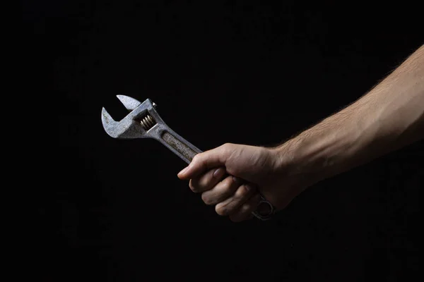 Adjustable wrench on a black background. Old work tool. A man\'s hand holds an adjustable wrench.