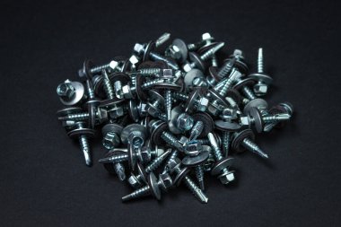 Roofing screws on a black background. Metal building material. Self-tapping screws for metal clipart
